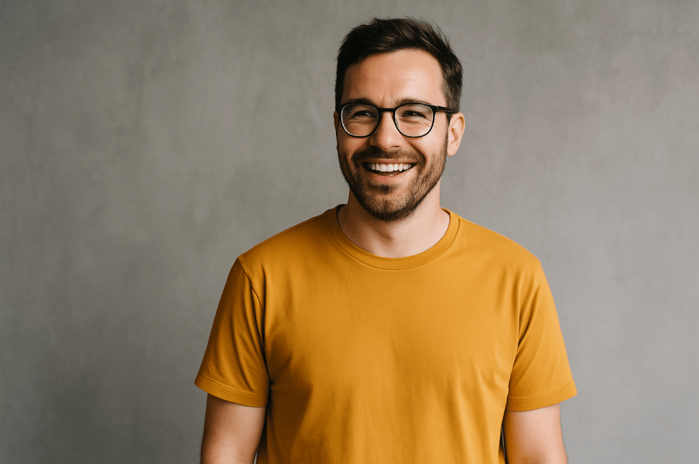 Man in mosterdgeel T-shirt lacht ontspannen voor een grijze muur: symbool voor loslaten van perfectionisme en het spotlight effect. 