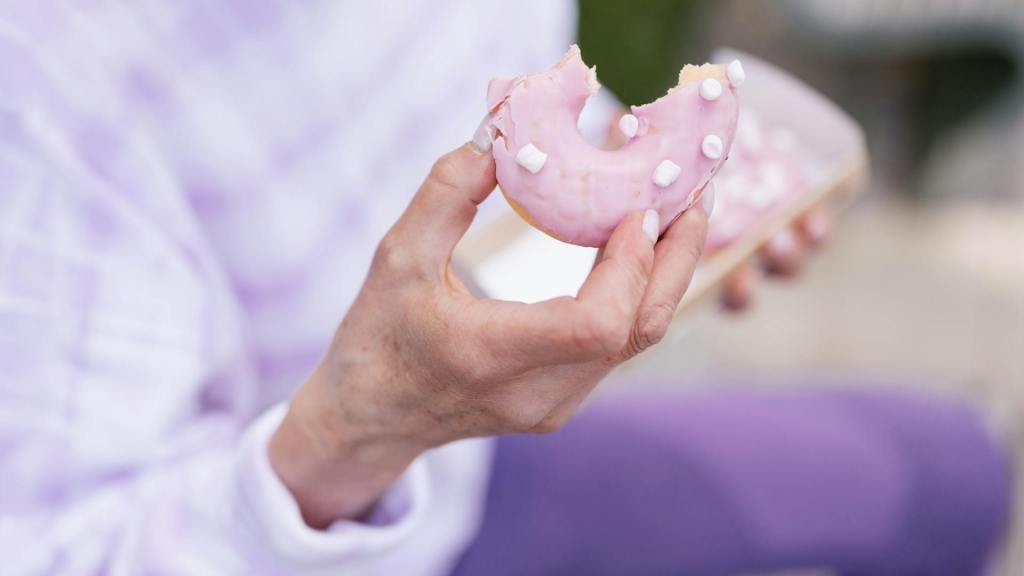 Hand houdt een half opgegeten roze donut vast – symbool voor uitstelgedrag, korte-termijn-genot en present bias in coaching