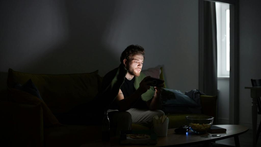 Man zit ’s avonds op de sofa en kijkt naar zijn smartphone, symbool voor digitale afleiding en dopamineverslaving – mental coach Wim Annerel over aandacht en focus