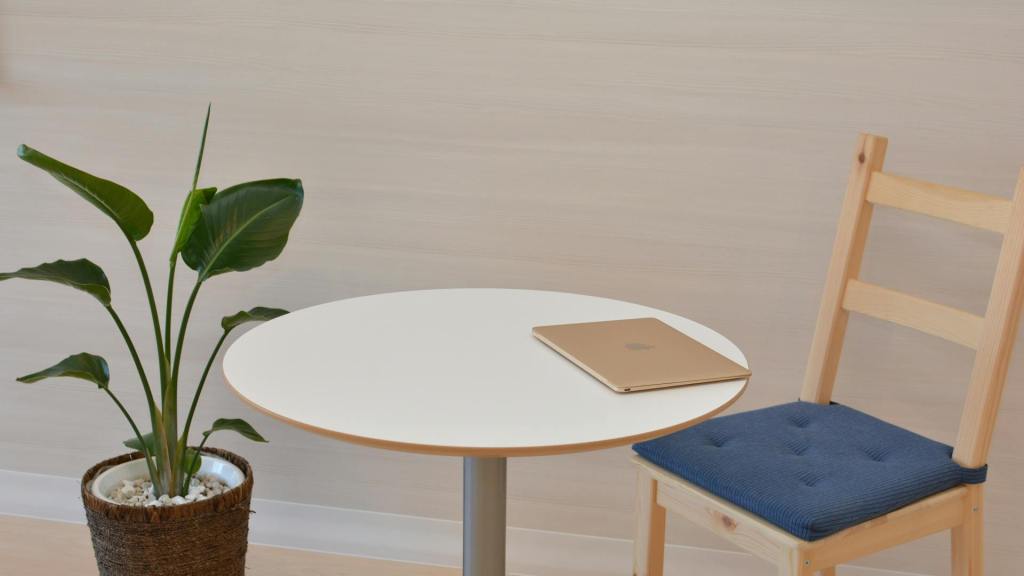 Minimalistische en opgeruimde werkplek met een gesloten laptop op een ronde witte tafel naast een plant, ideaal voor gefocust werken